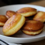 Deux madeleines moelleuses dorées, avec leur forme de coquille parfaite et leur texture fondante, présentées simplement sur une assiette.