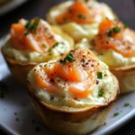 Mini cocottes gourmandes au saumon fumé et fromage frais, joliment dressées dans des moules en pâte croustillante, garnies de ciboulette et de poivre noir.