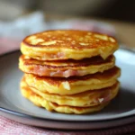 Pancakes salés au jambon et fromage empilés sur une assiette, bien dorés et moelleux, avec une garniture fondante visible entre les couches.